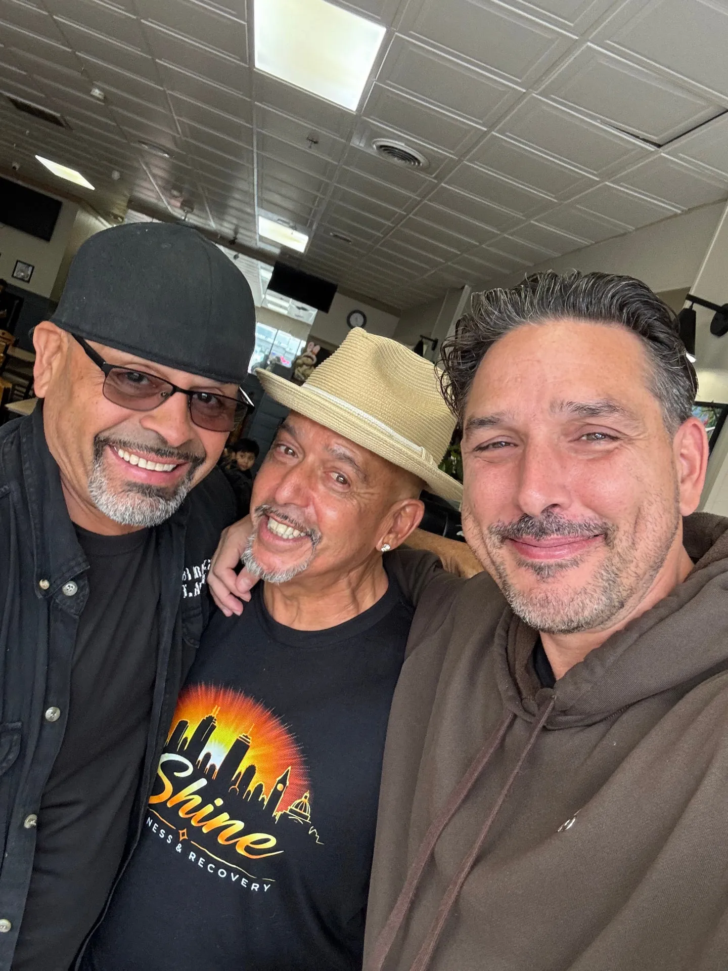 Rob G in a Shine Wellness t-shirt and fedora with two friends at a community gathering