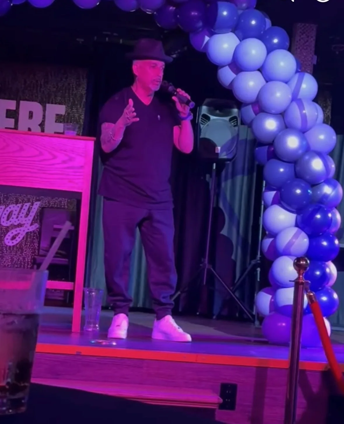 Rob G speaking on stage at a community recovery event with blue and purple balloons