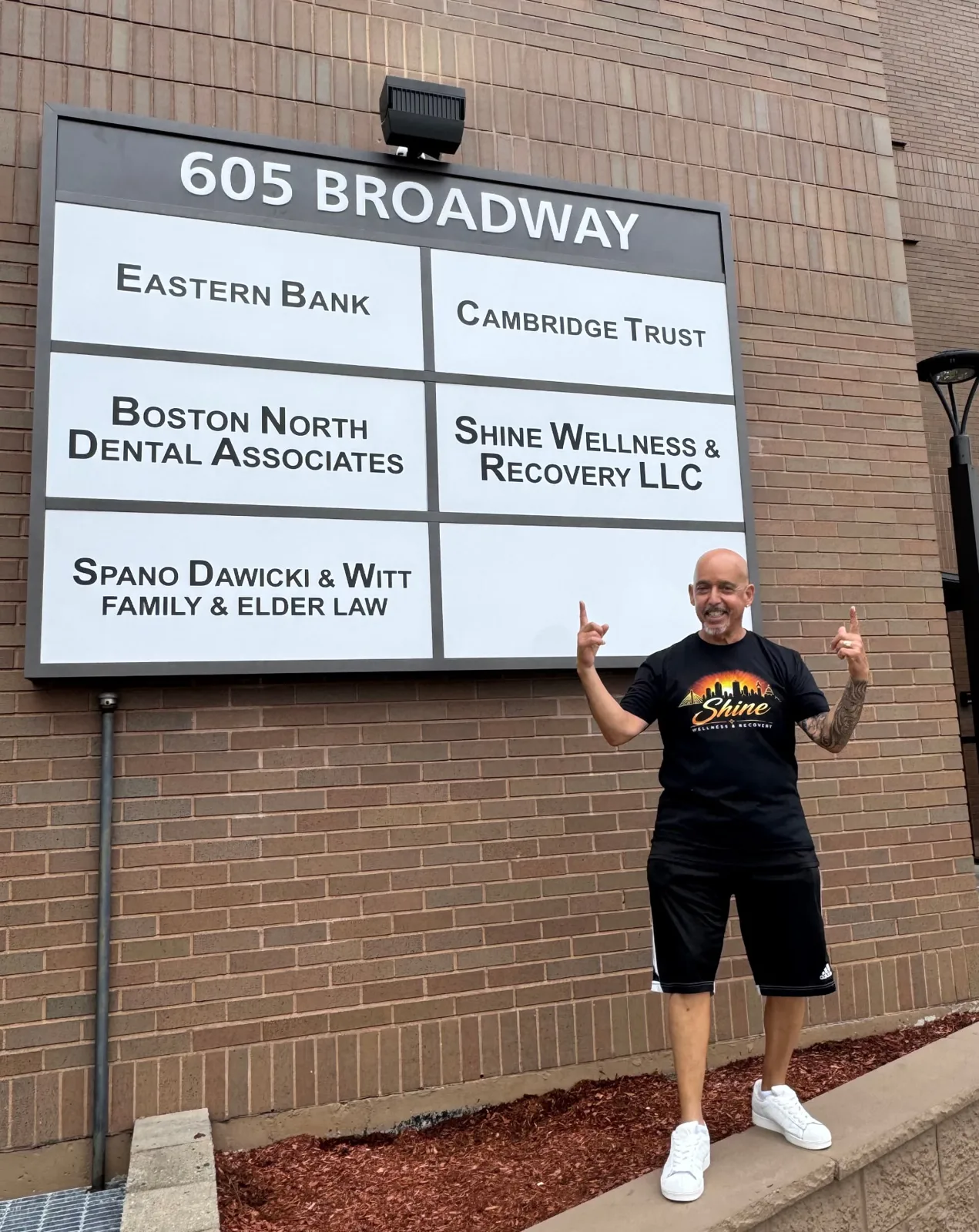 Shine Wellness & Recovery founder standing beside the 605 Broadway building directory sign in Saugus, MA