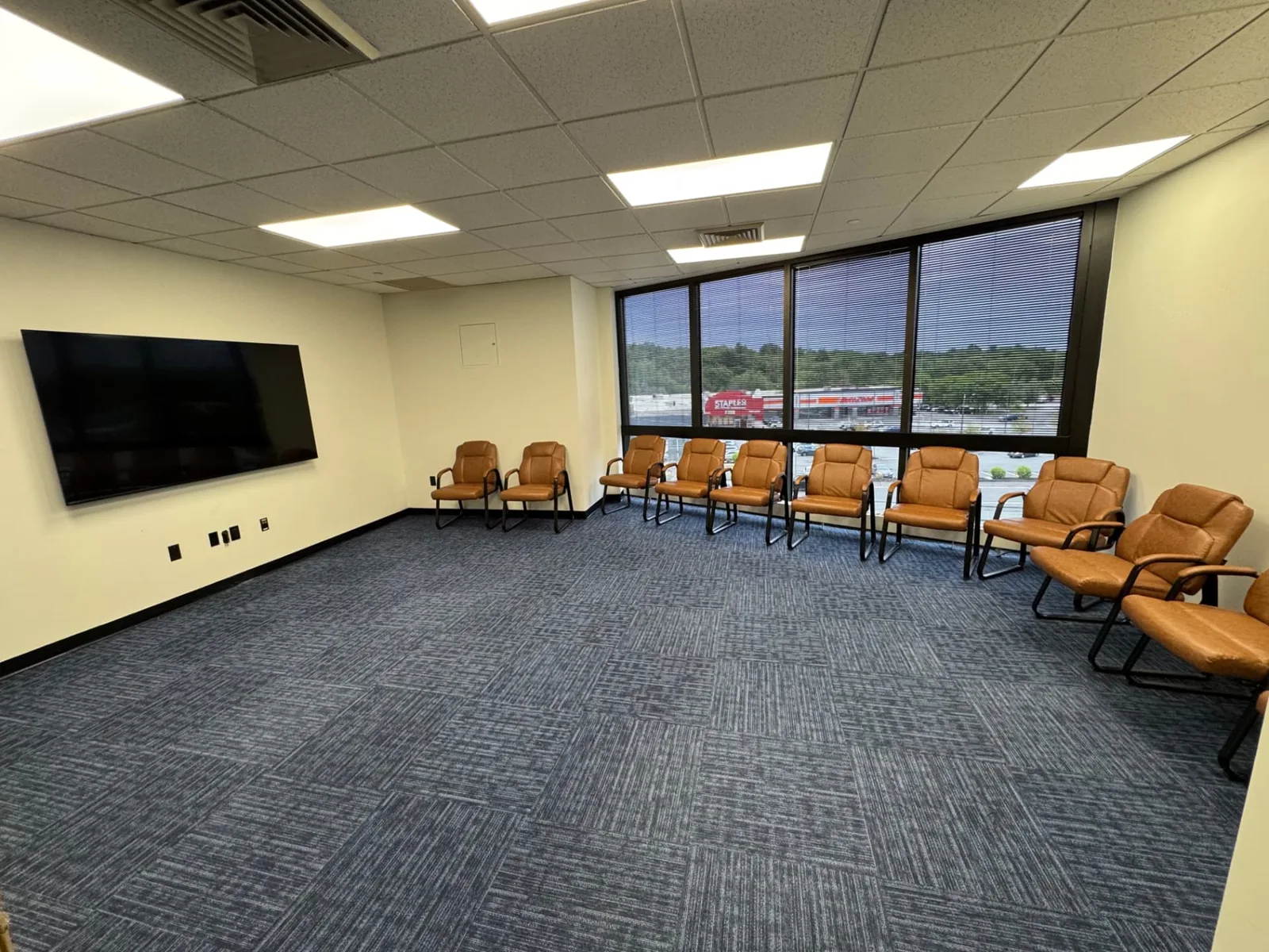 Group therapy room at Shine Wellness & Recovery with a circle of leather chairs, large windows, and a wall-mounted TV