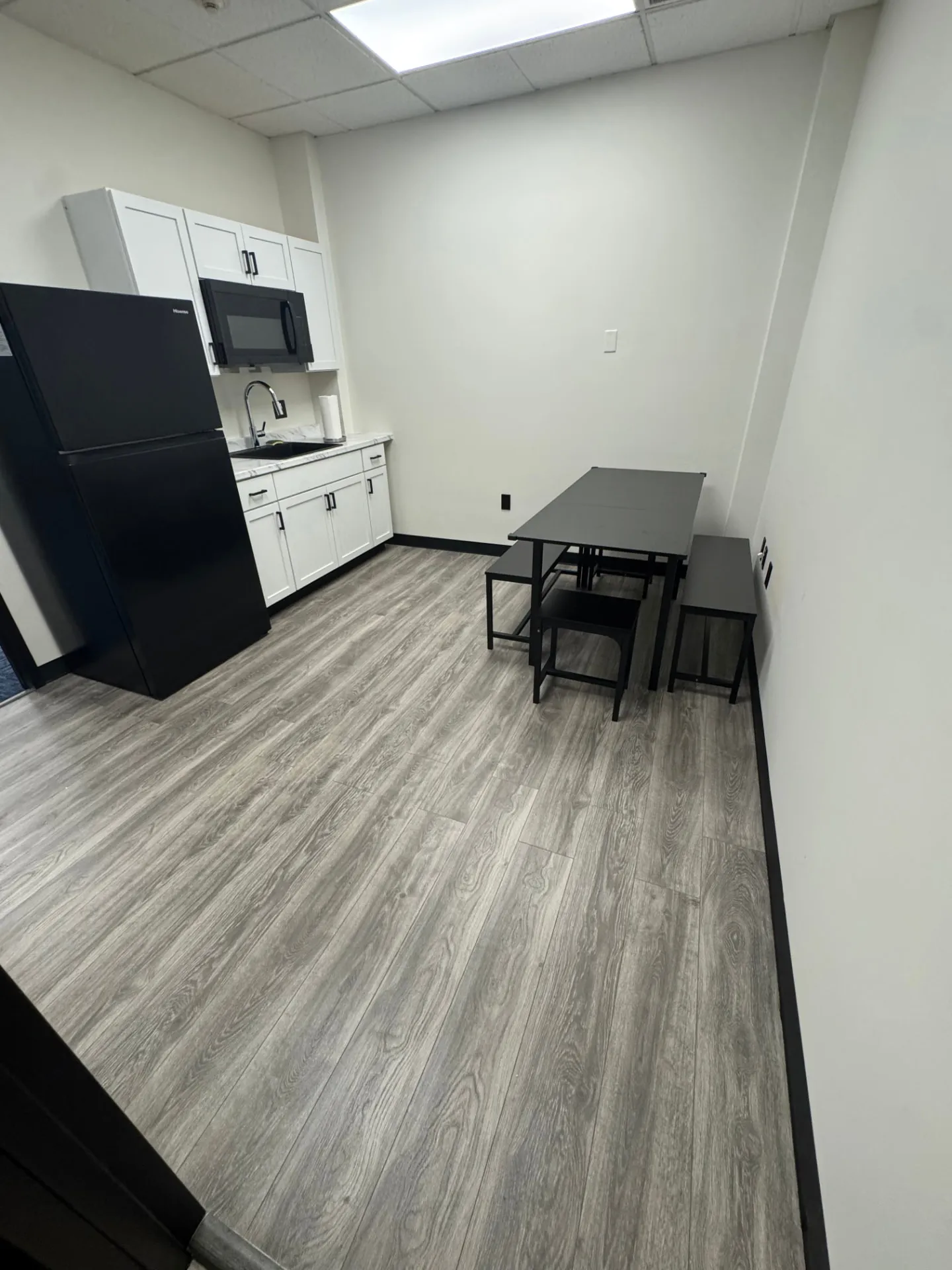 Breakroom at Shine Wellness & Recovery with a black dining table, matching benches and stools, white walls, and recessed lighting